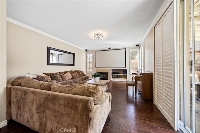 living area with baseboards, dark wood-style flooring, a glass covered fireplace, and crown molding