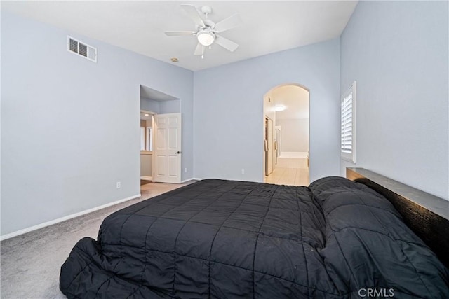 carpeted bedroom with arched walkways, visible vents, ensuite bathroom, ceiling fan, and baseboards