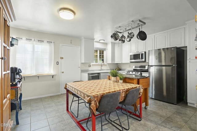 kitchen featuring baseboards, light tile patterned flooring, a sink, appliances with stainless steel finishes, and white cabinetry