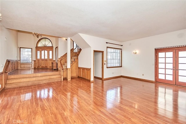 unfurnished living room with light wood finished floors, french doors, stairway, and a wealth of natural light