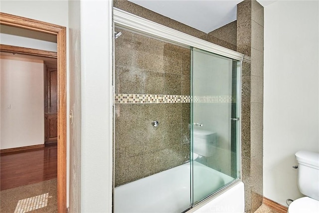 bathroom with toilet and shower / bath combination with glass door