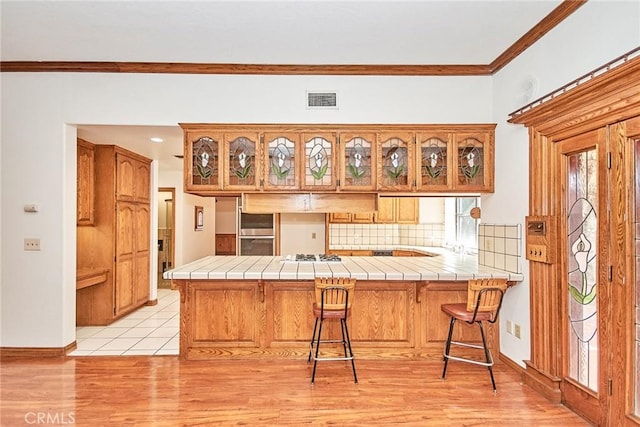 kitchen with visible vents, tile counters, a kitchen breakfast bar, a peninsula, and crown molding