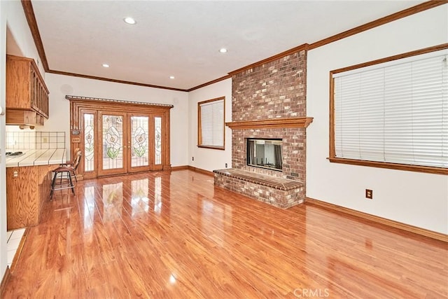 unfurnished living room with ornamental molding, a brick fireplace, french doors, and light wood finished floors