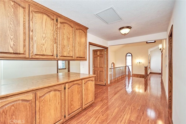 kitchen featuring a textured ceiling, light wood-style flooring, visible vents, baseboards, and brown cabinets