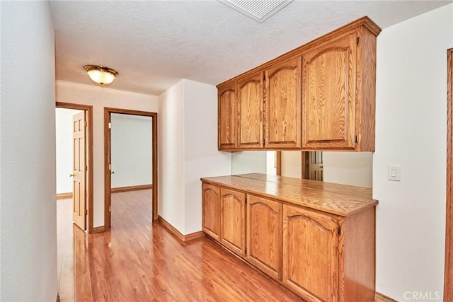 hallway featuring light wood-style flooring, a textured ceiling, visible vents, and baseboards