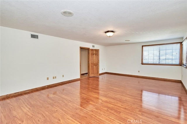 empty room featuring light wood-style floors, visible vents, a textured ceiling, and baseboards