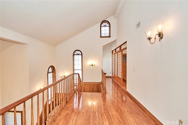 corridor with high vaulted ceiling, visible vents, an upstairs landing, and wood finished floors