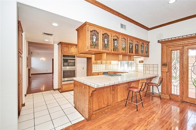 kitchen with visible vents, decorative backsplash, a peninsula, crown molding, and stainless steel double oven