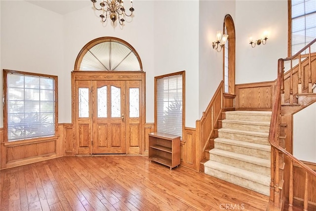 entrance foyer featuring a wainscoted wall, a notable chandelier, stairway, and light wood finished floors