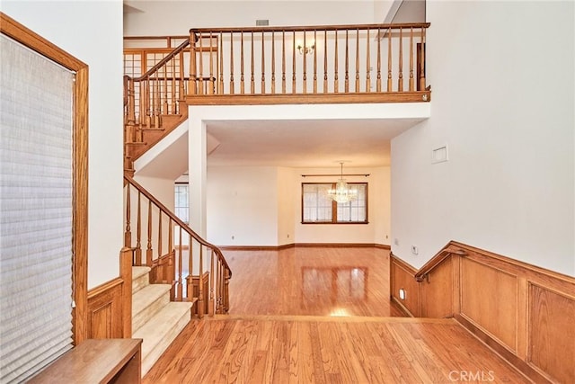 interior space featuring light wood finished floors, wainscoting, a high ceiling, stairs, and a chandelier