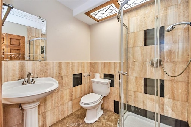 bathroom with toilet, a skylight, tile walls, wainscoting, and a stall shower