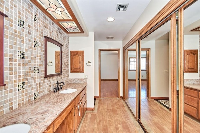 bathroom featuring wood finished floors, a sink, visible vents, decorative backsplash, and double vanity