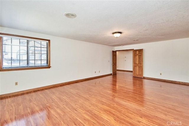 spare room featuring light wood-style flooring, baseboards, and a textured ceiling