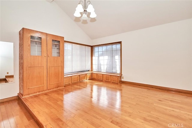 unfurnished room with high vaulted ceiling, light wood-type flooring, a notable chandelier, and baseboards