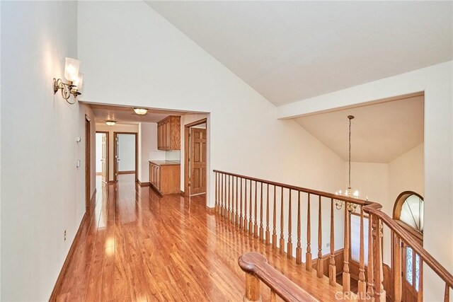 hallway with high vaulted ceiling, light wood-type flooring, a notable chandelier, and baseboards