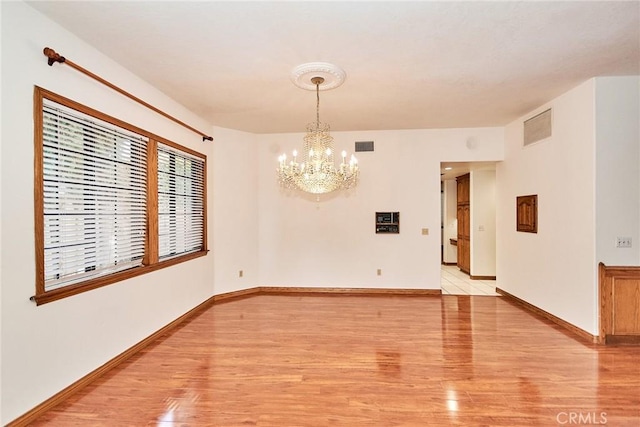 unfurnished room featuring light wood-type flooring, visible vents, a notable chandelier, and baseboards