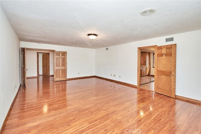 spare room featuring baseboards, visible vents, a textured ceiling, and light wood finished floors