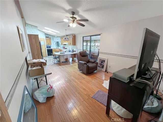 living area with a ceiling fan, lofted ceiling, and light wood finished floors