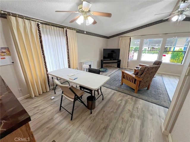 dining room with baseboards, a ceiling fan, lofted ceiling, light wood-style flooring, and a textured ceiling