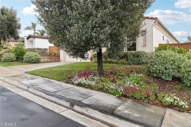 view of front facade with an attached garage, concrete driveway, a tiled roof, stucco siding, and a front lawn