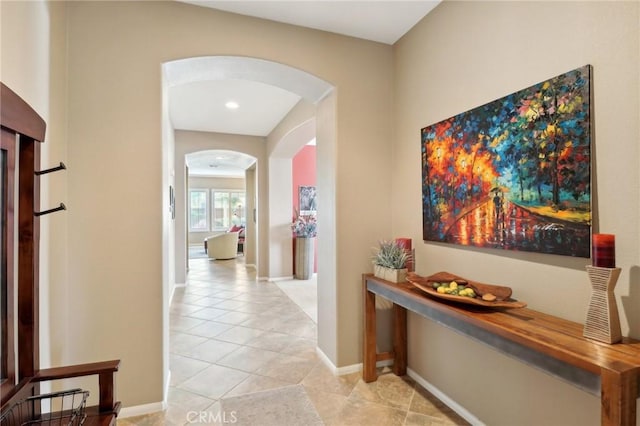 hallway with arched walkways, light tile patterned floors, and baseboards