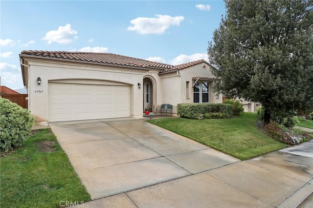 mediterranean / spanish house with a garage, a front yard, a tiled roof, and stucco siding