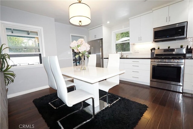 kitchen with baseboards, dark wood finished floors, appliances with stainless steel finishes, white cabinetry, and backsplash