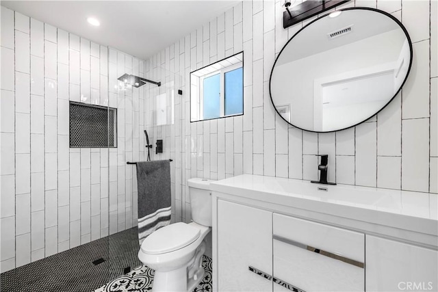 full bathroom with visible vents, toilet, vanity, a walk in shower, and tile walls