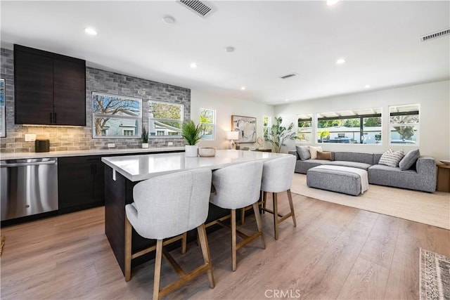 kitchen with dishwasher, light countertops, a kitchen bar, and visible vents