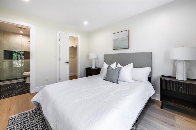 bedroom featuring connected bathroom, wood finished floors, visible vents, baseboards, and a walk in closet