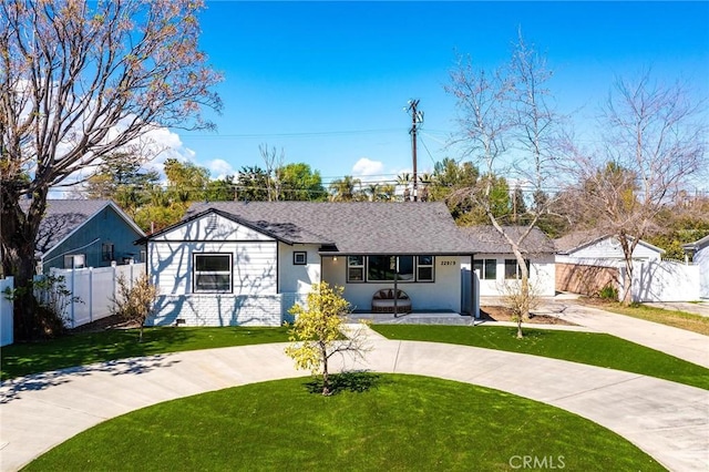 view of front of property with driveway, roof with shingles, fence, and a front yard