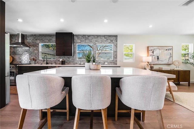 interior space featuring light wood-style flooring, recessed lighting, visible vents, and wall chimney range hood