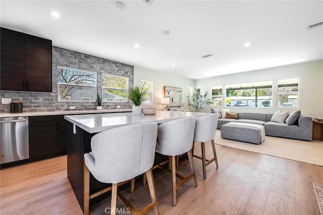 kitchen featuring visible vents, dishwasher, a breakfast bar area, light countertops, and light wood-type flooring