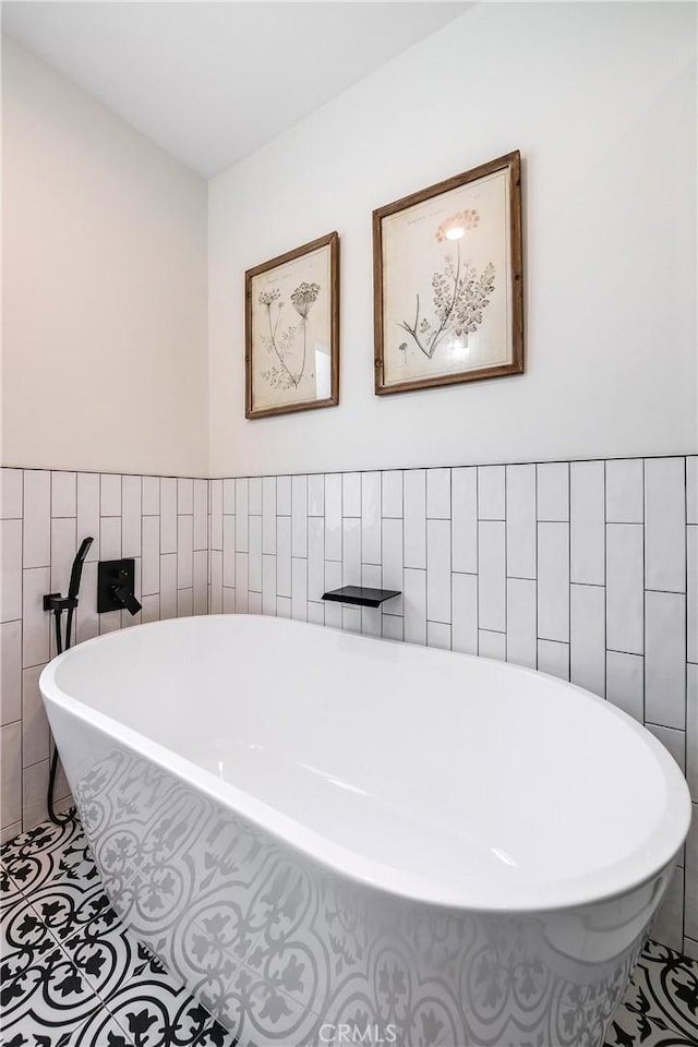 bathroom with a freestanding bath, a wainscoted wall, tile patterned flooring, and tile walls