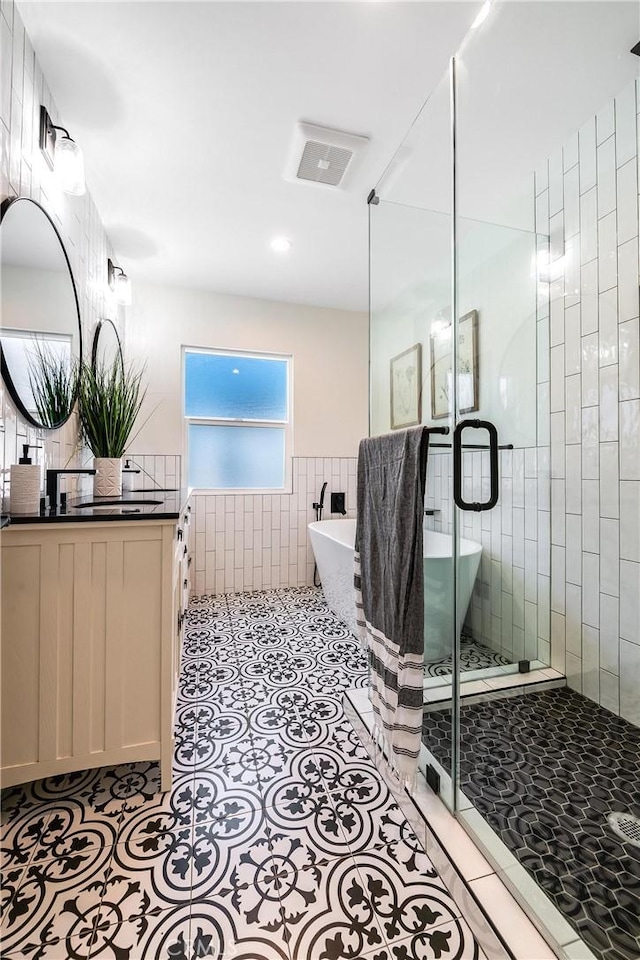 full bathroom featuring visible vents, a soaking tub, tile patterned floors, vanity, and tile walls