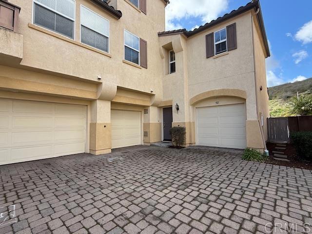 view of front of home featuring decorative driveway, a tile roof, an attached garage, and stucco siding