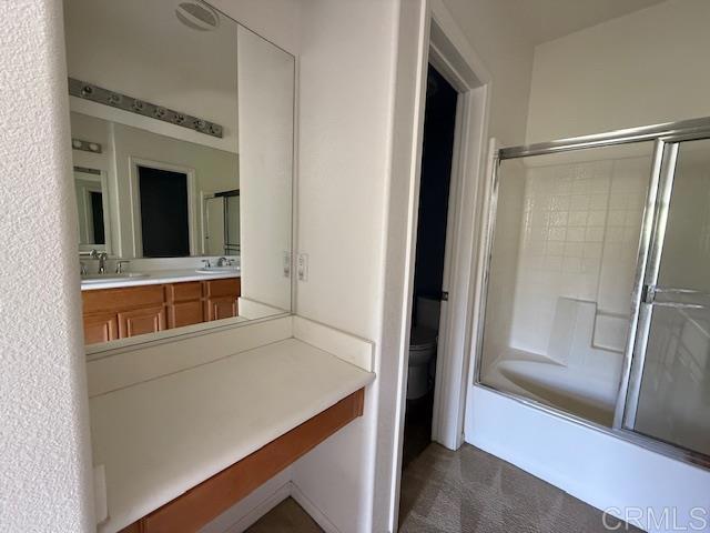 bathroom with double vanity, toilet, combined bath / shower with glass door, and a sink