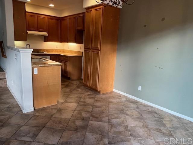 kitchen with baseboards, brown cabinetry, recessed lighting, and under cabinet range hood