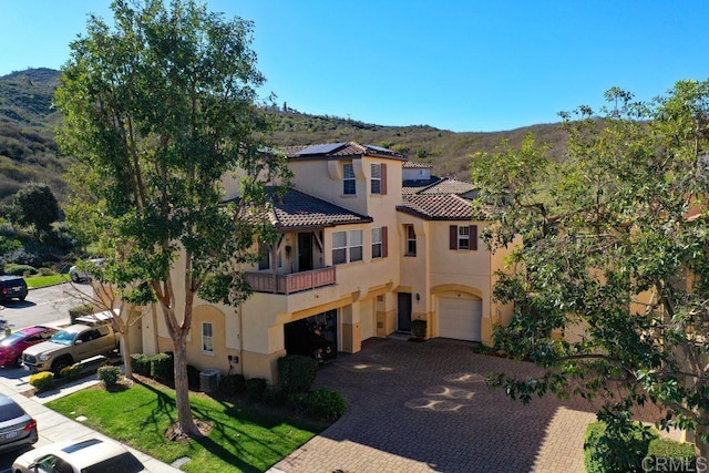 mediterranean / spanish home featuring central AC unit, a balcony, an attached garage, roof mounted solar panels, and stucco siding