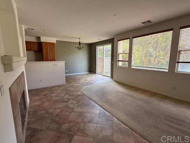 unfurnished living room featuring baseboards, carpet, visible vents, and an inviting chandelier