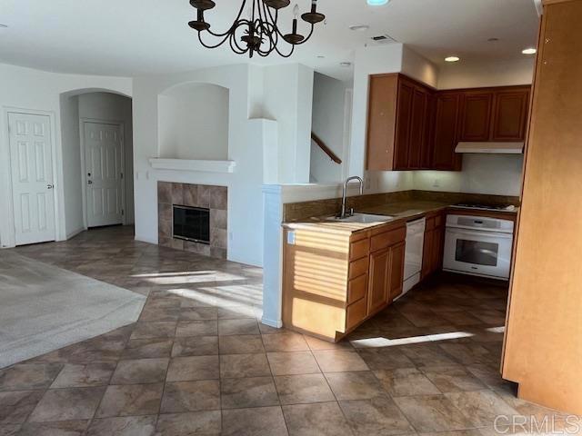 kitchen featuring white appliances, a tiled fireplace, an inviting chandelier, under cabinet range hood, and a sink