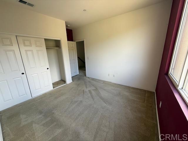 unfurnished bedroom with light carpet, visible vents, and a closet