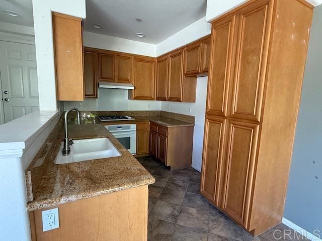 kitchen with a sink, gas cooktop, a peninsula, oven, and under cabinet range hood