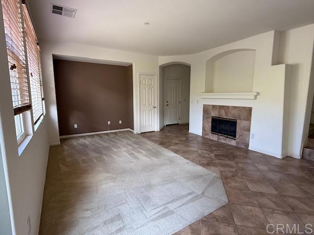 unfurnished living room with baseboards, visible vents, and a tile fireplace