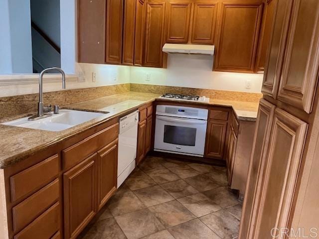 kitchen featuring light countertops, brown cabinetry, a sink, white appliances, and under cabinet range hood