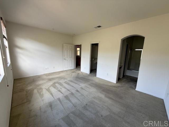 unfurnished bedroom featuring carpet floors, ensuite bath, a spacious closet, and arched walkways