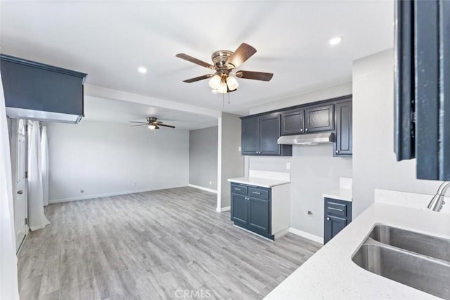kitchen featuring baseboards, ceiling fan, under cabinet range hood, light wood-style floors, and a sink