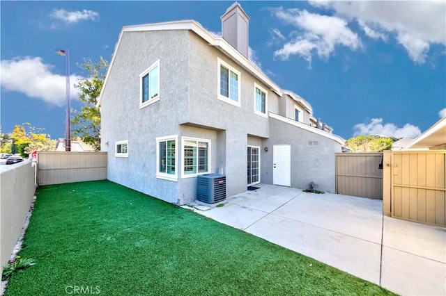 back of property with central AC unit, a fenced backyard, a lawn, stucco siding, and a patio area