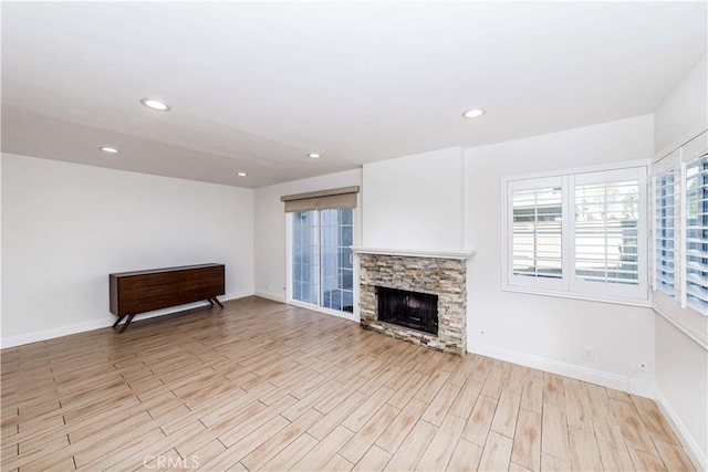 unfurnished living room with light wood-type flooring, recessed lighting, baseboards, and a stone fireplace