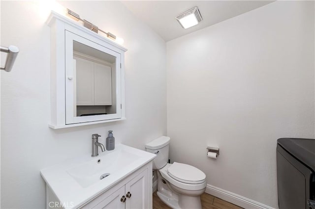 half bath with toilet, wood finished floors, visible vents, vanity, and washer / clothes dryer